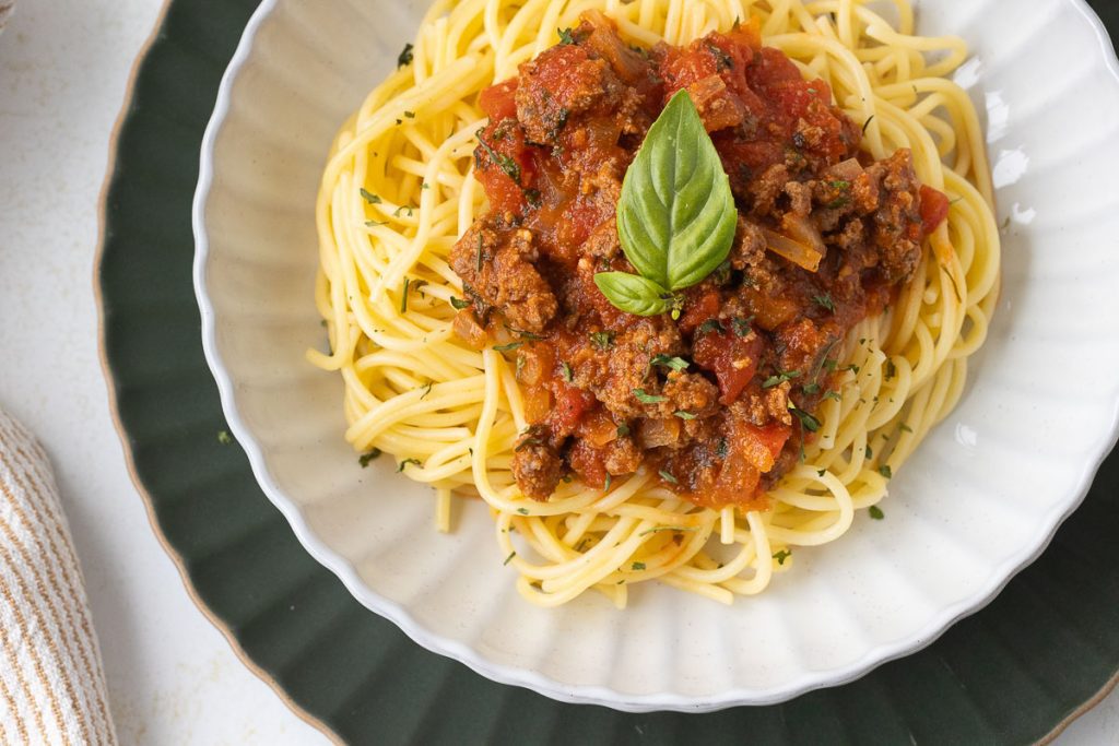 Serving bowl with pasta and italian sauce with ground beef on the top.