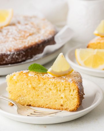 Whole lemon olive oil cake with a golden top and soft, tender crumb, lightly dusted with powdered sugar and displayed on a serving platter.