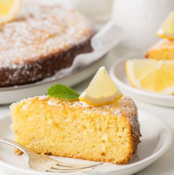 Lemon olive oil cake with a golden surface and delicate crumb, lightly sprinkled with powdered sugar and presented on a serving platter.