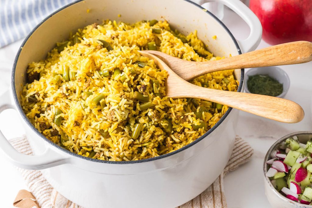 pot full of lubia polo with serving spoons