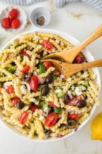 Greek pasta salad with feta cheese, cucumbers, tomatoes, olives, and fusilli pasta in a large serving bowl.