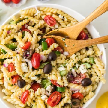 Greek pasta salad with feta cheese, cucumbers, tomatoes, olives, and fusilli pasta in a large serving bowl.