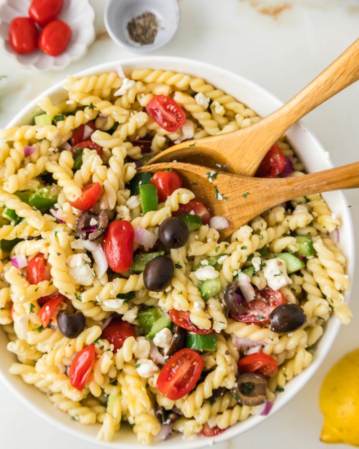 Greek pasta salad with feta cheese, cucumbers, tomatoes, olives, and fusilli pasta in a large serving bowl.