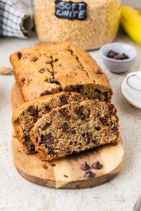 Moist banana bread loaf made with freshly milled flour, sliced and served on a wooden cutting board.