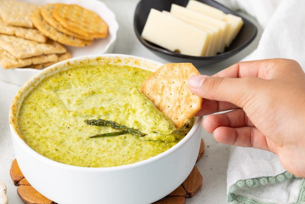 Scooping up Baked asparagus with the cracker in the bowl.