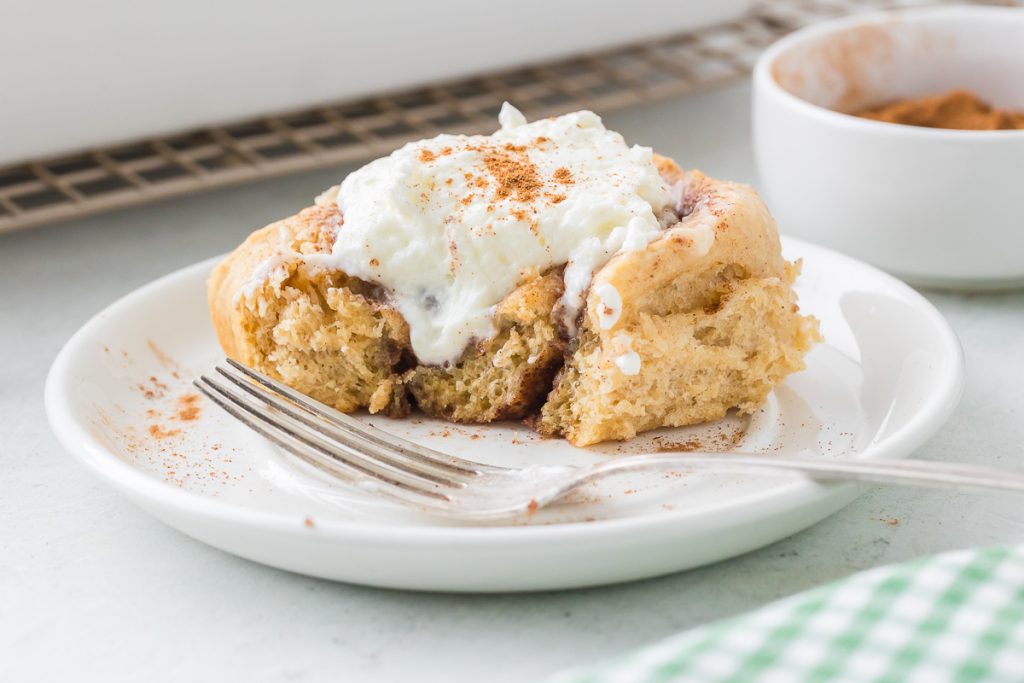 cinnamon roll with icing on the small plate sprinkled with ground cinnamon