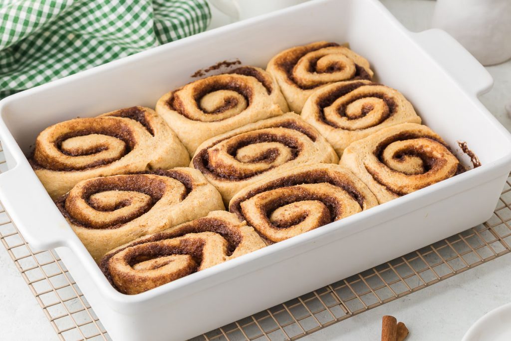 Cinnamon rolls baked in the baking pan cooling down on cooling rack. 